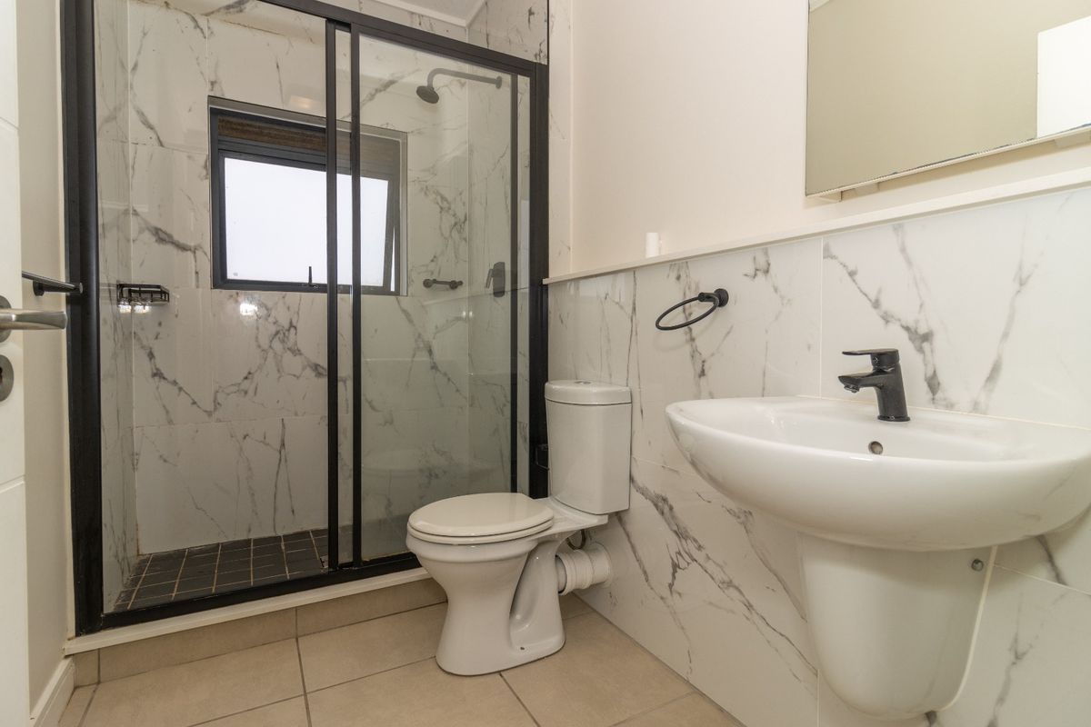 Modern bathroom featuring a walk-in shower with black-framed glass enclosure, marble-look wall tiling, pedestal basin, and contemporary black fixtures.