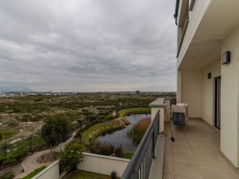 A spacious balcony featuring tiled flooring and a metal balustrade, offering expansive views over the surrounding landscape and natural pond area.