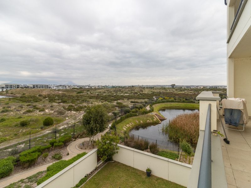 A spacious balcony featuring tiled flooring and a metal balustrade, offering expansive views over the surrounding landscape and natural pond area.