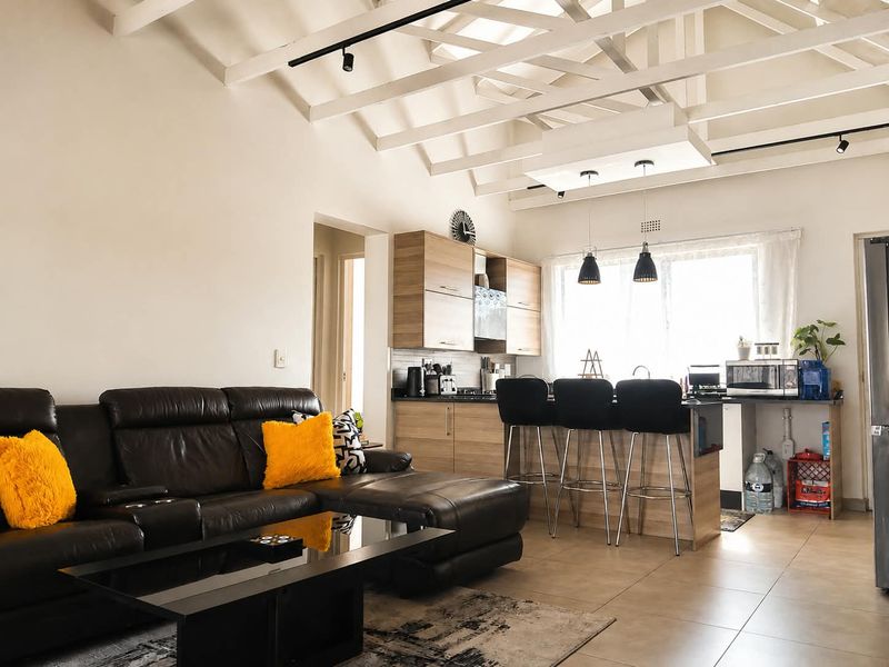 Open-plan living area featuring a modern kitchen with wood-finish cabinetry, a breakfast island, and high vaulted ceilings with exposed timber beams.