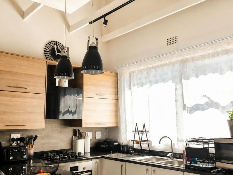 Modern kitchen featuring light wood and white cabinetry, granite countertops, gas hob, built-in oven, and striking exposed timber ceiling beams.
