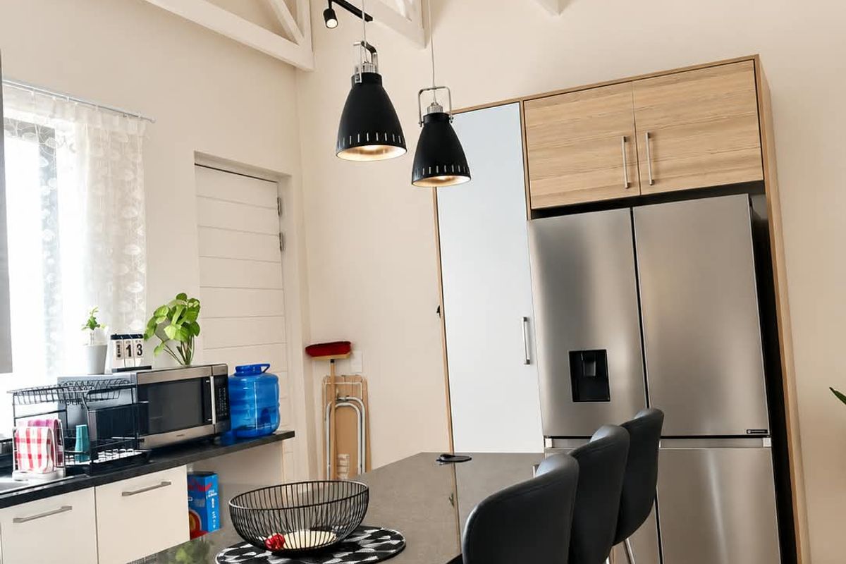 Modern kitchen featuring granite countertops, light wood cabinetry, exposed white roof trusses, and stylish pendant lighting in an open-plan layout.