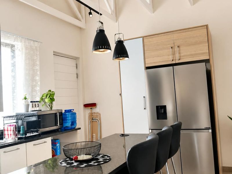 Modern kitchen featuring granite countertops, light wood cabinetry, exposed white roof trusses, and stylish pendant lighting in an open-plan layout.