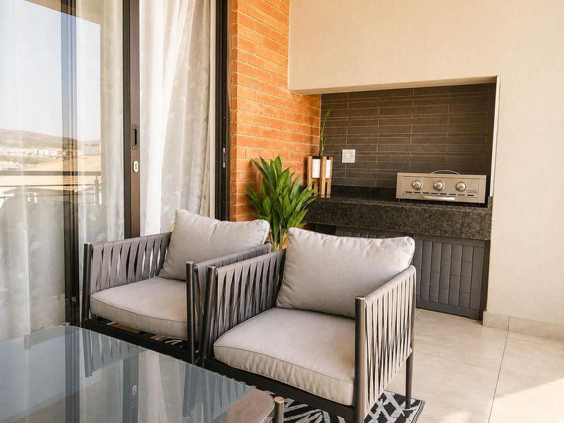 Covered balcony featuring a built-in braai with granite countertop, exposed brick accents, and large sliding glass doors leading to the interior.