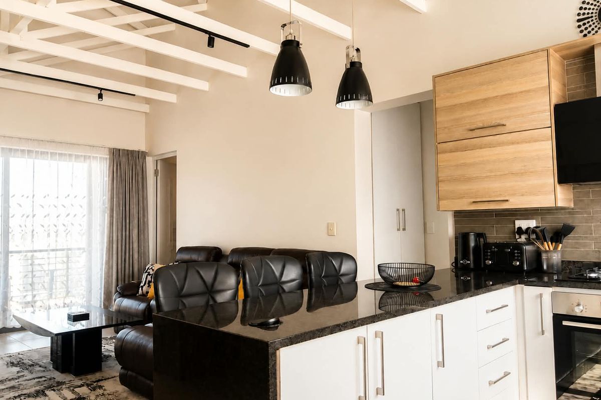 Modern open-plan kitchen and living area featuring exposed ceiling beams, granite countertops, built-in appliances, and direct access to a balcony.