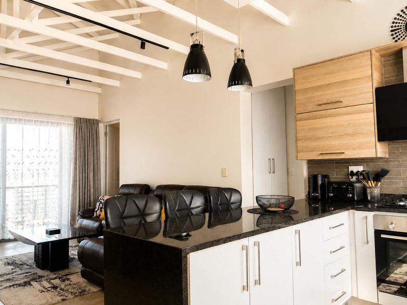 Modern open-plan kitchen and living area featuring exposed ceiling beams, granite countertops, built-in appliances, and direct access to a balcony.