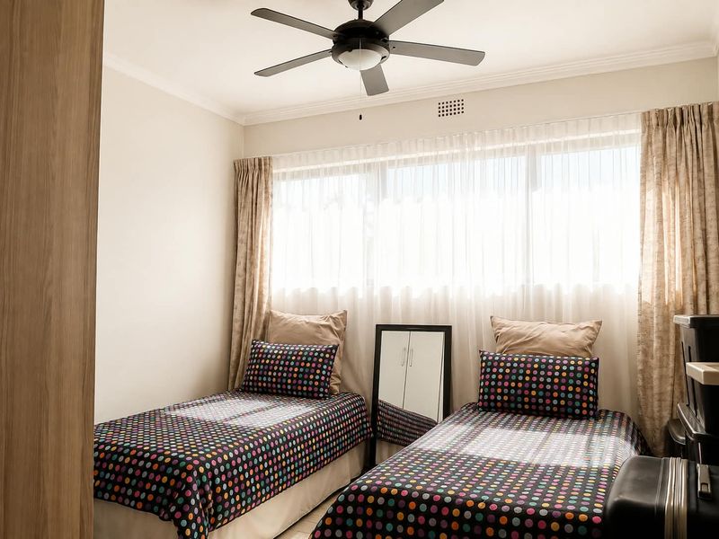 A well-lit bedroom featuring a ceiling fan, built-in cupboard storage, and large windows with curtain tracks.
