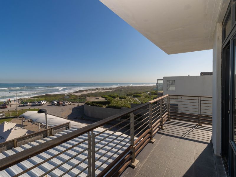 A spacious balcony featuring tiled flooring and a modern metal and timber railing, offering expansive coastal and ocean views.