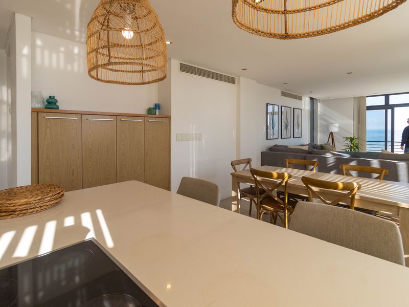 Modern open-plan living and kitchen area featuring a stone island, built-in cabinetry, and ducted air conditioning with views toward the ocean.