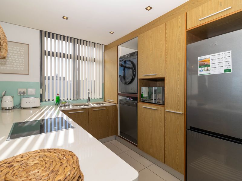 Modern kitchen featuring wood-finish cabinetry, stone countertops, integrated appliances, and a sleek hob, offering a functional and contemporary cooking space.