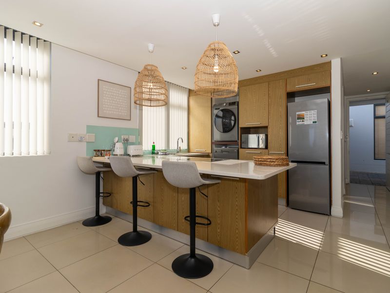 Modern kitchen featuring a central island with stone countertops, built-in cabinetry, integrated appliances, and tiled flooring, offering a functional and contemporary cooking space.