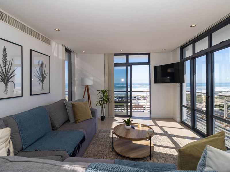 Bright and modern living room featuring large aluminium-framed sliding glass doors that offer expansive ocean views and provide access to the balcony.