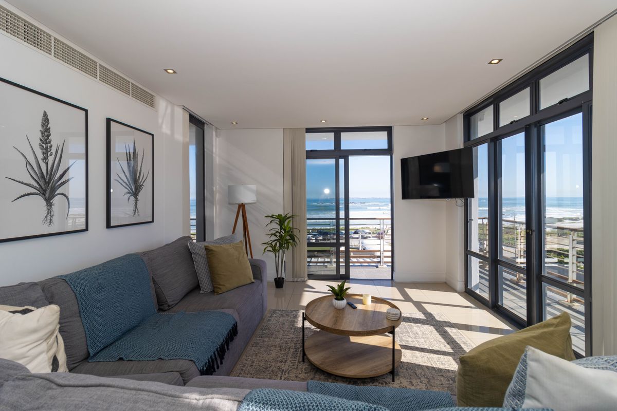 Bright and modern living room featuring large aluminium-framed sliding glass doors that offer expansive ocean views and provide access to the balcony.