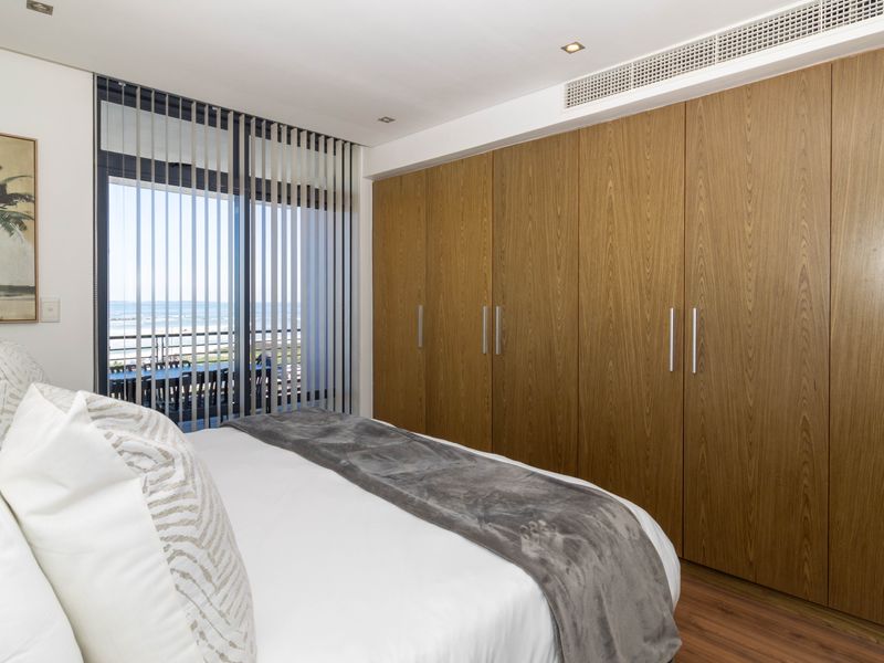Modern bedroom featuring extensive built-in wooden cupboards, ducted air conditioning, and a sliding glass door leading to a balcony with ocean views.