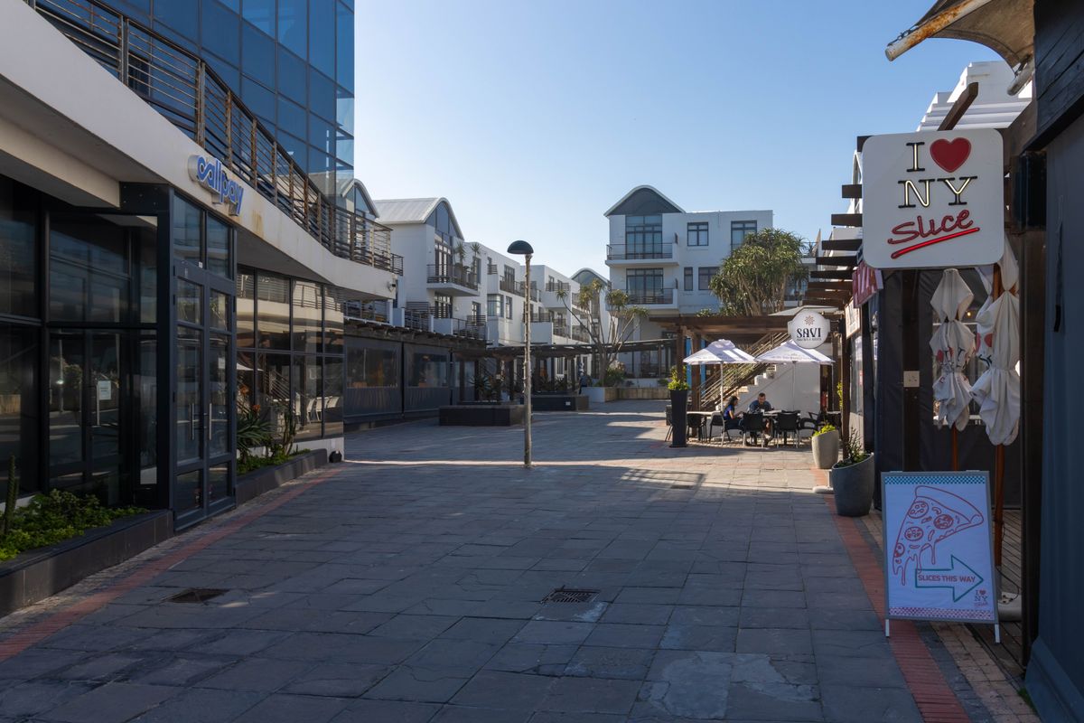 A view of a paved outdoor commercial and residential walkway featuring modern glass facades, balconies, and established outdoor seating areas.