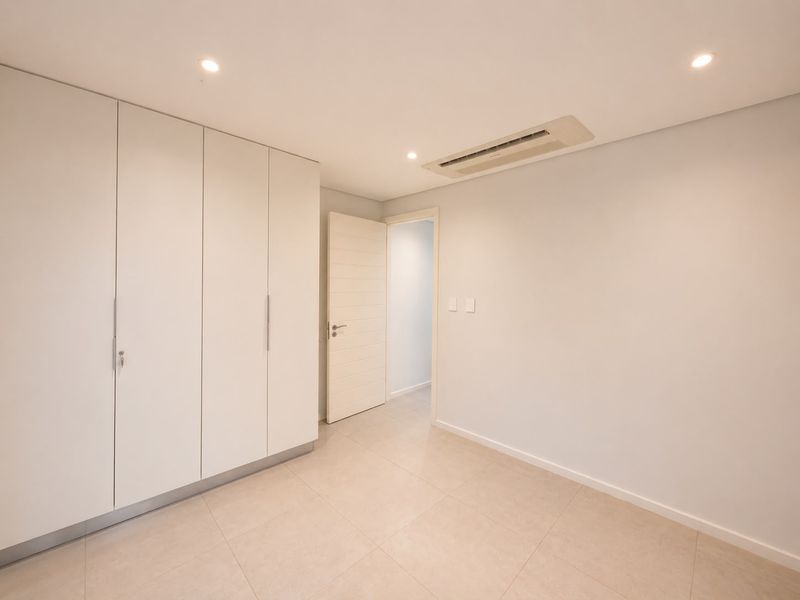 A clean, modern, and empty bedroom featuring built-in cupboards, tiled flooring, and integrated ducted air conditioning.