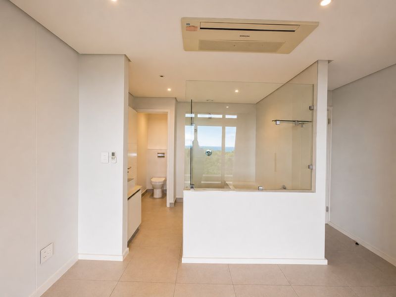 Modern open-plan bathroom featuring a glass-enclosed shower, wall-mounted toilet, and integrated ducted air conditioning, finished with neutral floor tiles.