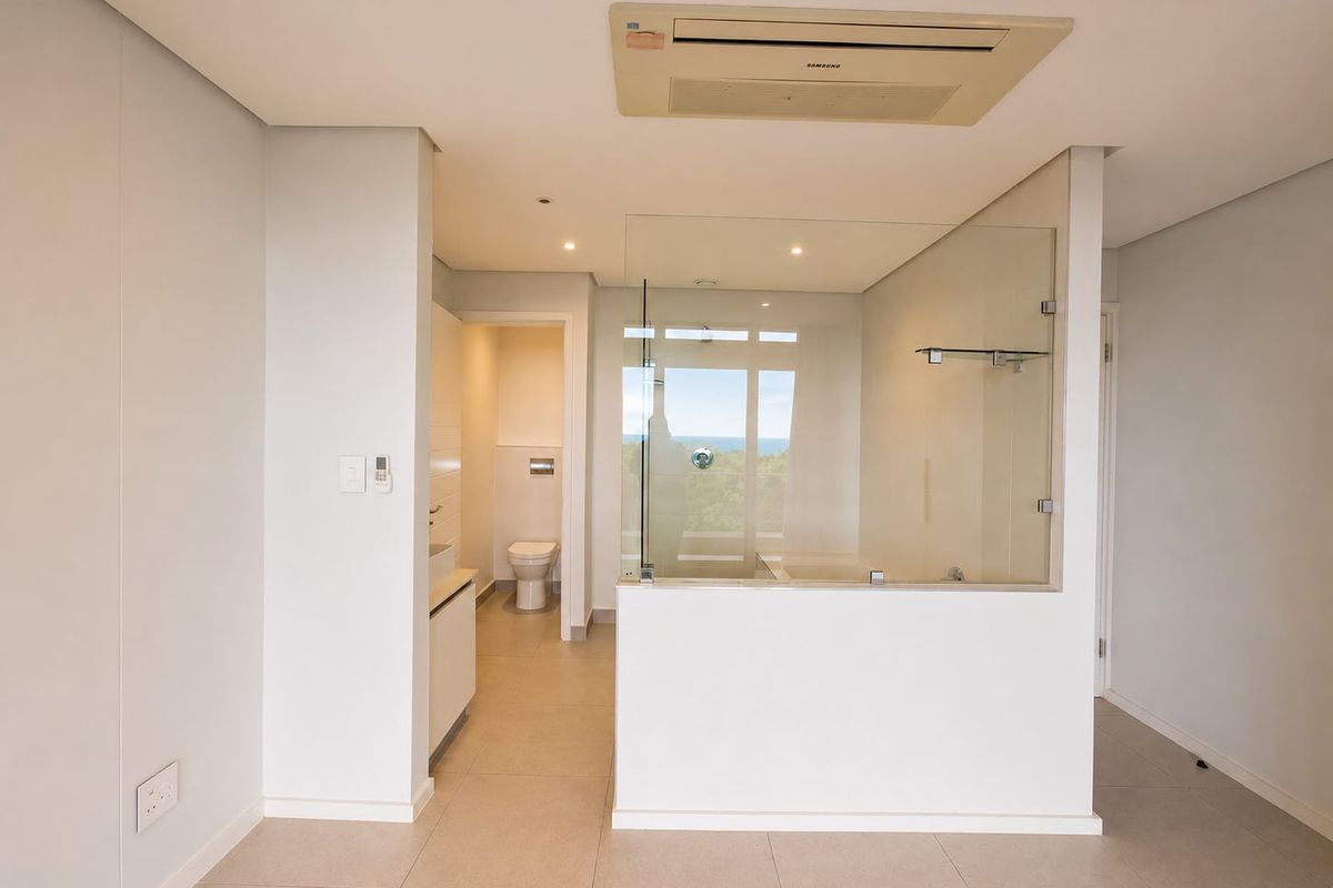 Modern open-plan bathroom featuring a glass-enclosed shower, wall-mounted toilet, and integrated ducted air conditioning, finished with neutral floor tiles.