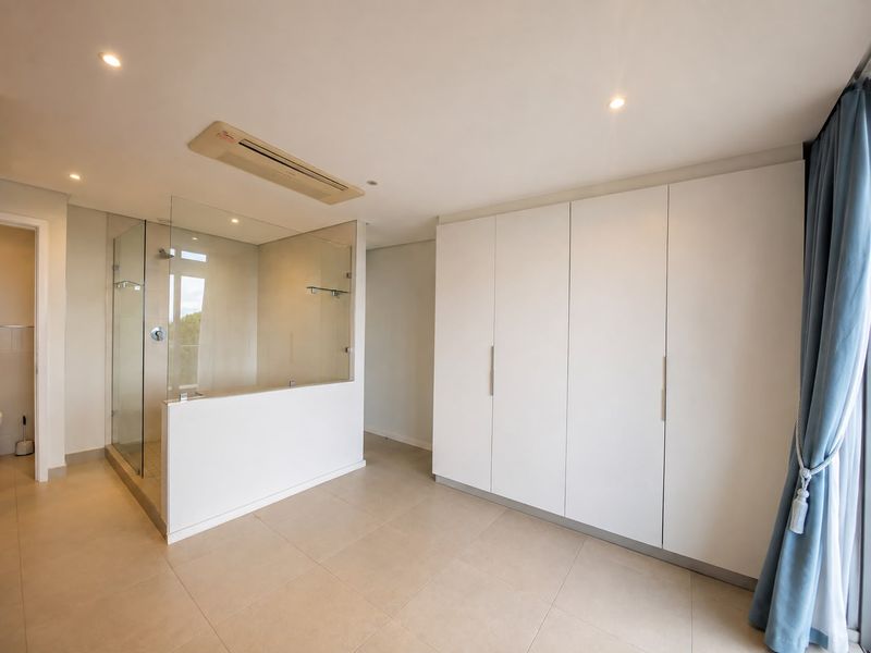 Spacious bedroom featuring built-in cupboards, tiled flooring, recessed lighting, ducted air conditioning, and an integrated glass-enclosed shower area.