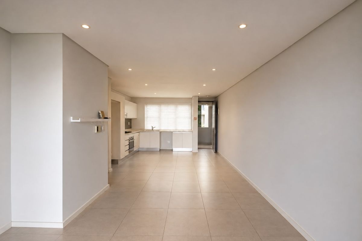 A spacious, open-plan living and kitchen area featuring neutral tiled flooring, recessed lighting, and a modern kitchen with built-in appliances.