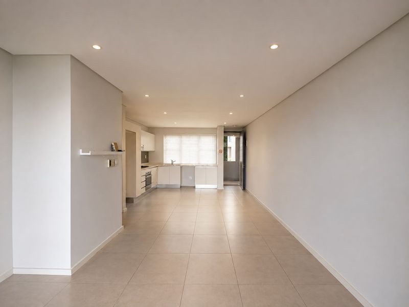 A spacious, open-plan living and kitchen area featuring neutral tiled flooring, recessed lighting, and a modern kitchen with built-in appliances.