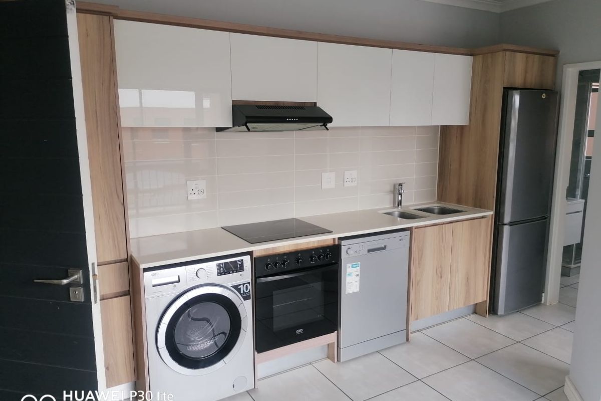 Modern kitchen featuring sleek white and wood-grain cabinetry, stone countertops, integrated electric hob, oven, extractor fan, and tiled flooring.