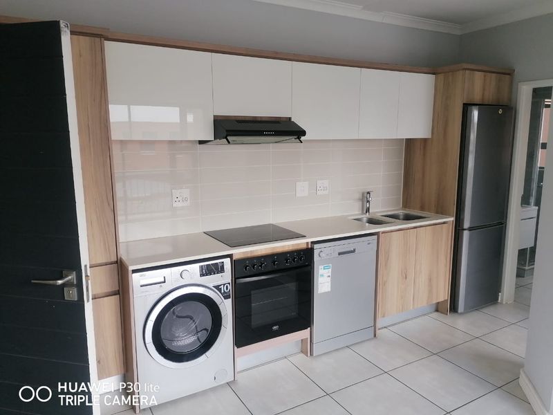 Modern kitchen featuring sleek white and wood-grain cabinetry, stone countertops, integrated electric hob, oven, extractor fan, and tiled flooring.