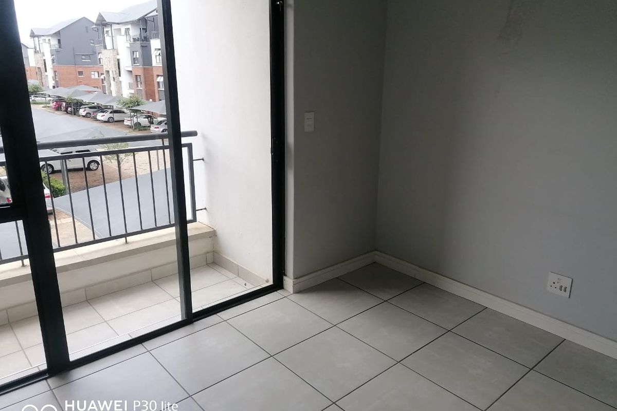 An empty living area featuring neutral tiled flooring, a sliding glass door leading to a balcony, and access to natural light.