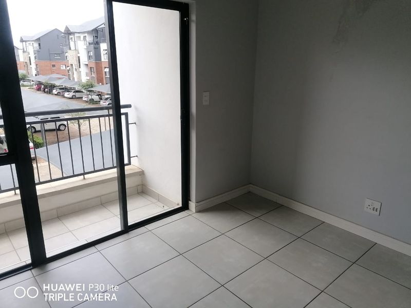 An empty living area featuring neutral tiled flooring, a sliding glass door leading to a balcony, and access to natural light.