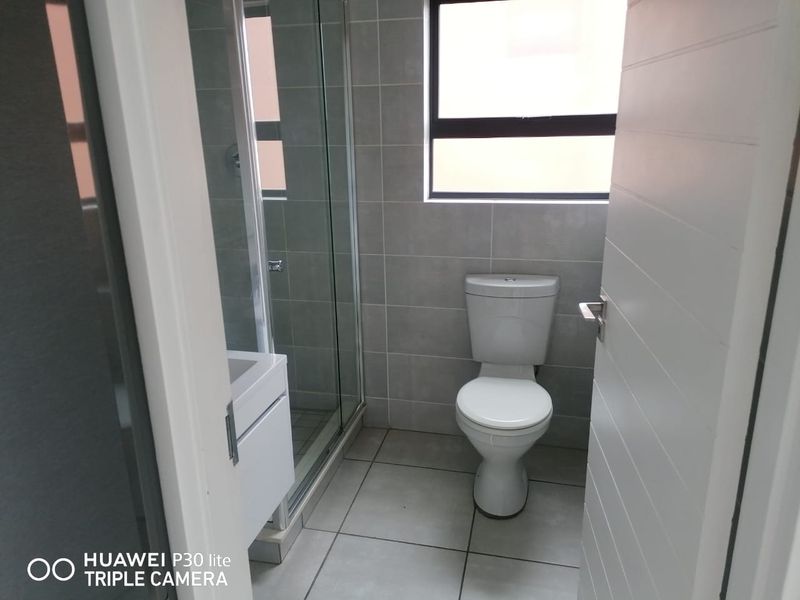 A clean, modern bathroom featuring a glass-enclosed shower, a white vanity cabinet, and neutral grey floor-to-ceiling wall tiles.