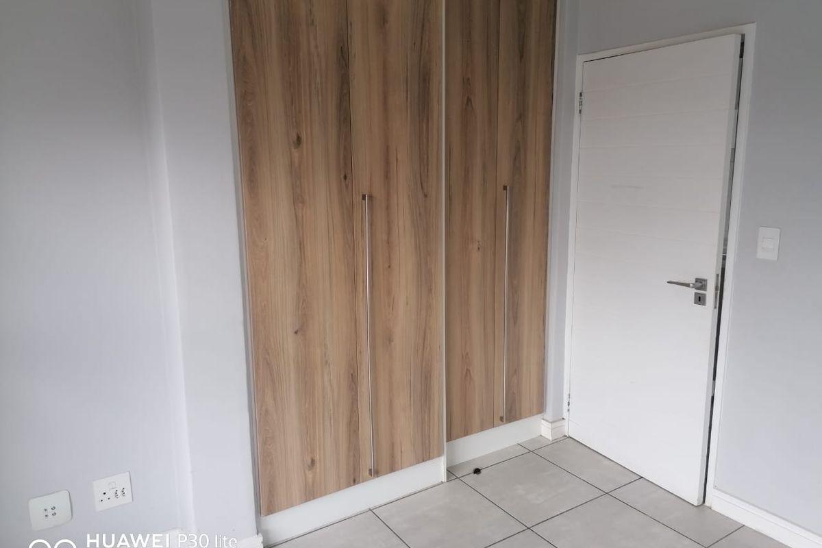 A clean, empty bedroom featuring modern wood-finish built-in cupboards, neutral tiled flooring, and a white internal door.