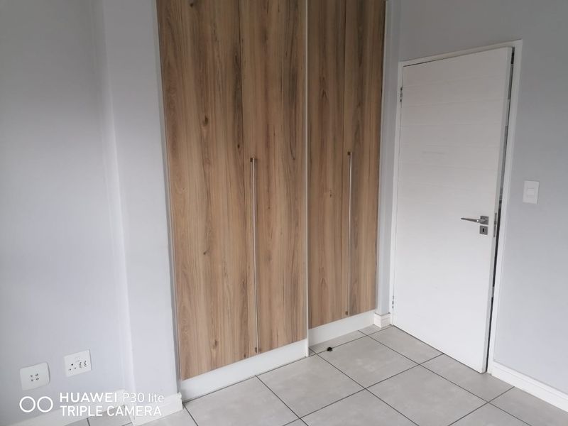 A clean, empty bedroom featuring modern wood-finish built-in cupboards, neutral tiled flooring, and a white internal door.