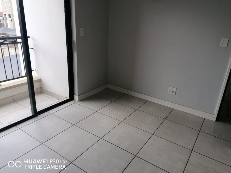 An empty living area featuring neutral floor tiles, grey walls, and a sliding glass door providing access to a balcony.