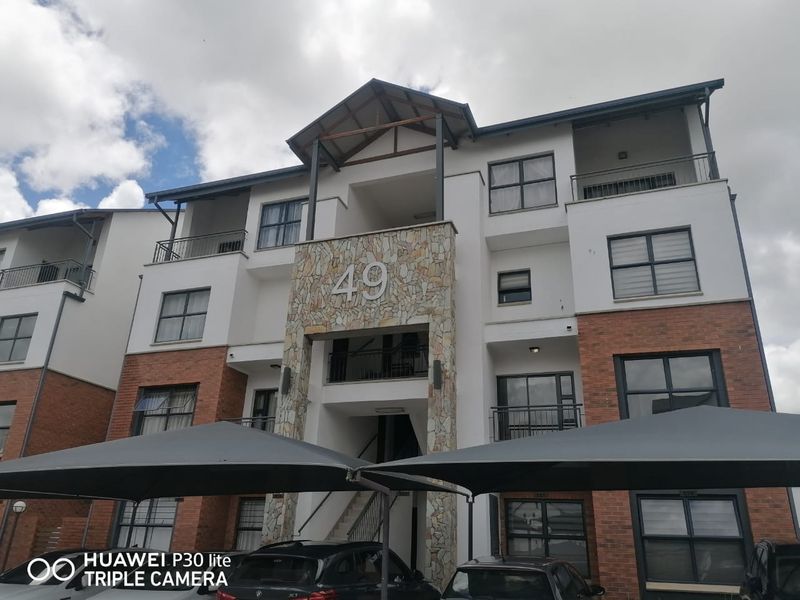 Front elevation of a multi-story apartment complex featuring stone cladding, brick accents, and private balconies with metal railings.