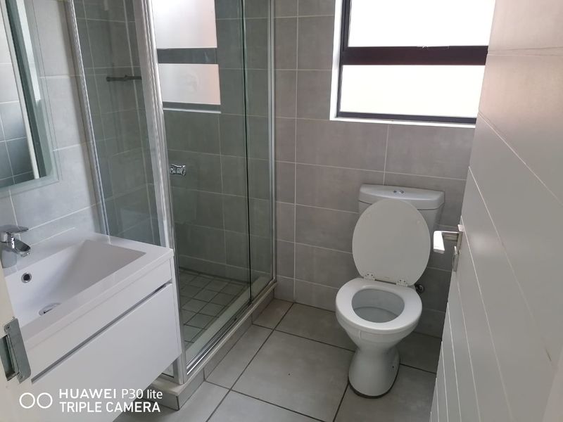 A clean, modern bathroom featuring a glass shower enclosure, vanity basin, and toilet with neutral grey wall and floor tiling.