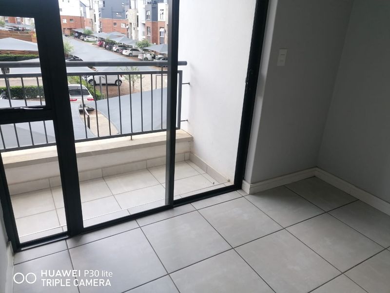 A clean, tiled balcony area accessible via a sliding glass door, featuring a metal balustrade and views over the complex parking area.