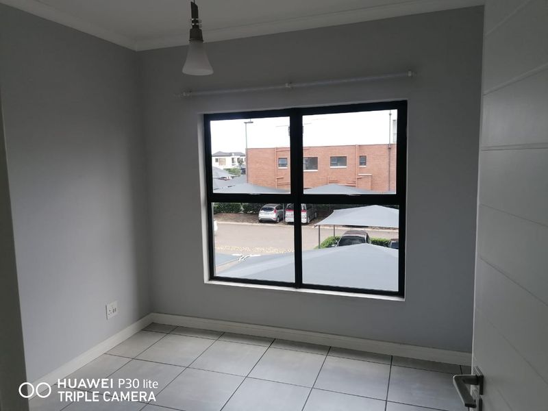 A clean, empty bedroom featuring neutral grey walls, tiled flooring, and a large aluminium-framed window with a view of the parking area.