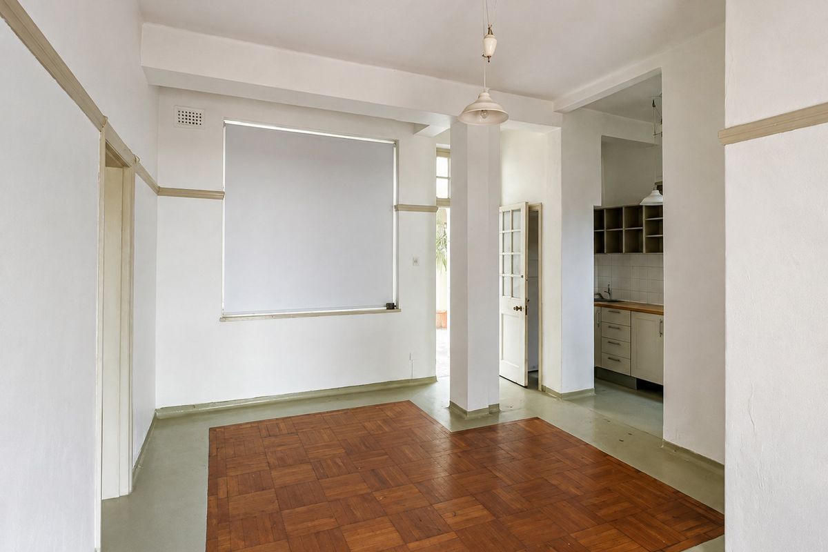 An open-plan living area featuring parquet flooring, neutral walls, and an adjoining kitchen space with built-in cabinetry and sink.