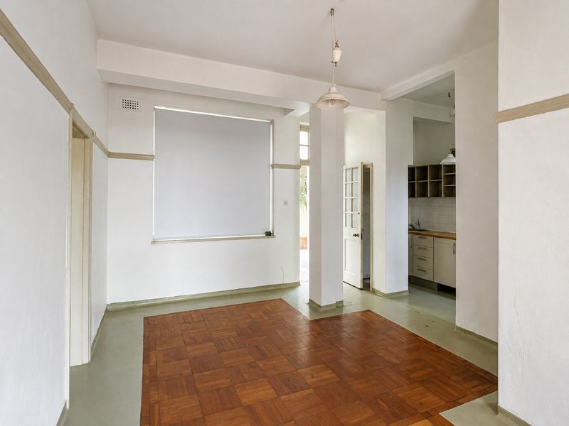 An open-plan living area featuring parquet flooring, neutral walls, and an adjoining kitchen space with built-in cabinetry and sink.