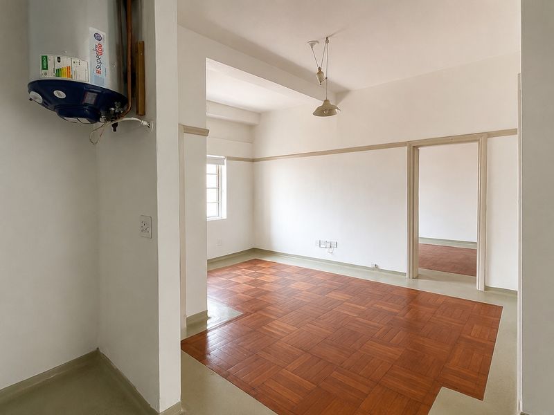 An empty living area featuring classic parquet flooring, neutral walls with picture rails, and an integrated electric water heater.