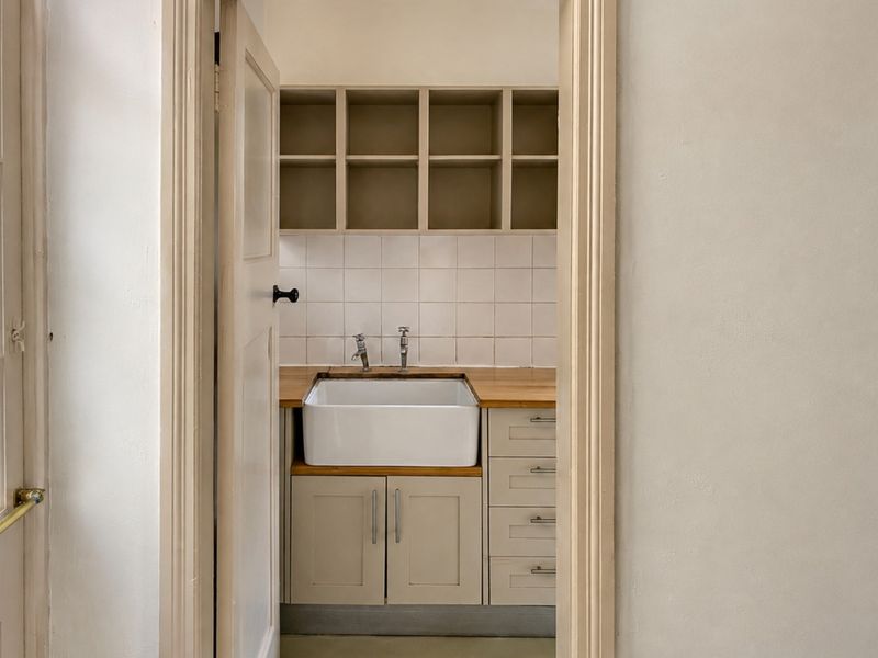 A clean and functional scullery or utility area featuring a classic farmhouse sink, wooden countertop, and ample built-in cabinetry with open shelving.