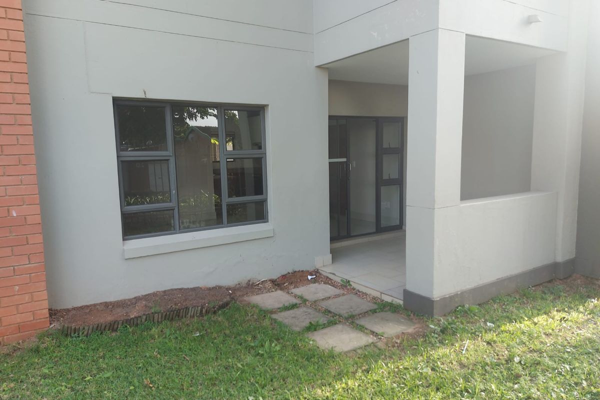 Rear exterior view of the apartment featuring a covered patio, sliding glass doors, and aluminium window frames with a small garden area.