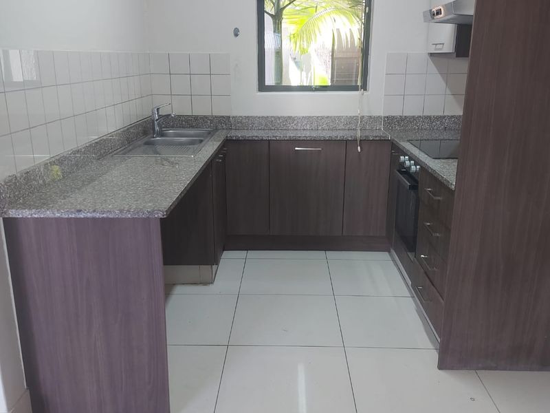 A functional U-shaped kitchen featuring granite countertops, built-in oven, hob, extractor fan, and ample cabinetry with a tiled splashback.