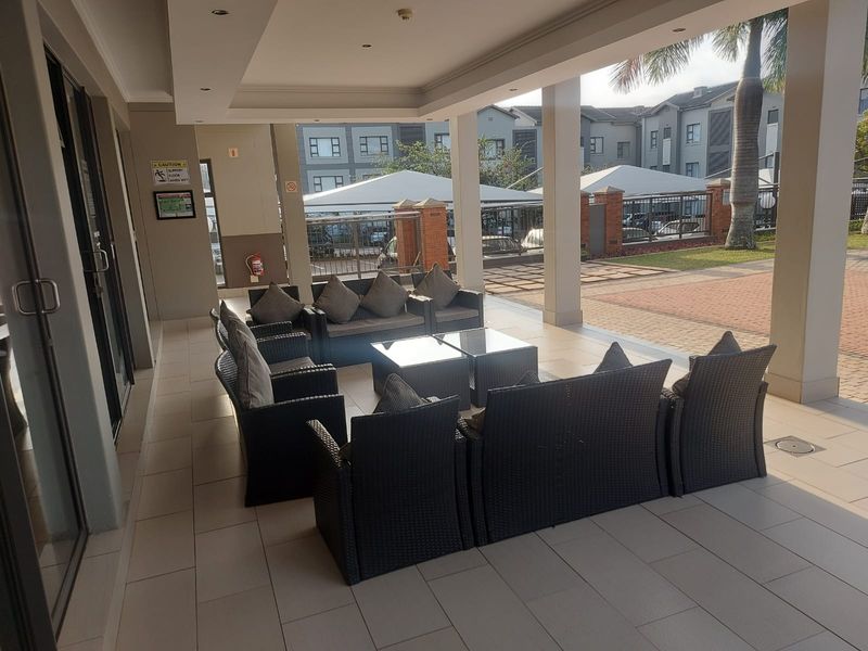 A spacious covered patio area featuring tiled flooring, recessed lighting, and structural support columns, providing a comfortable outdoor seating space.
