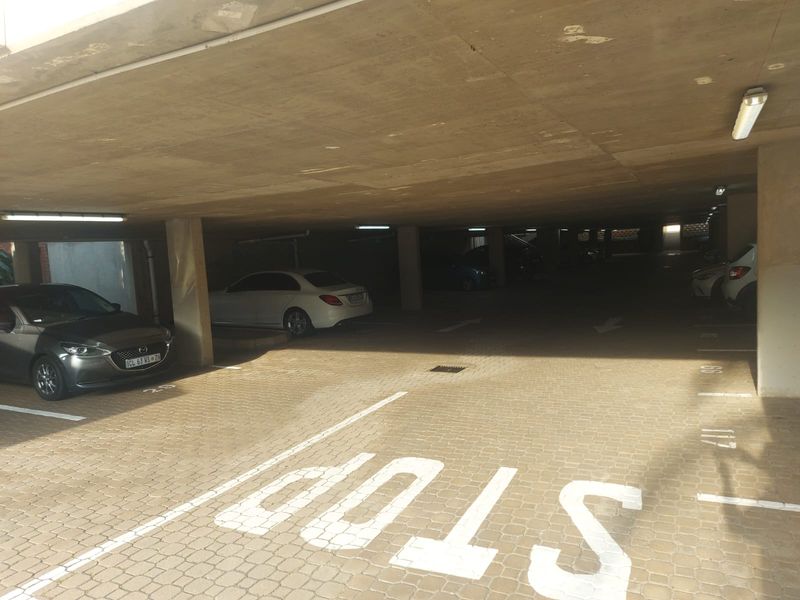 A covered parking garage area featuring concrete ceilings, support columns, and paved flooring with marked parking bays.