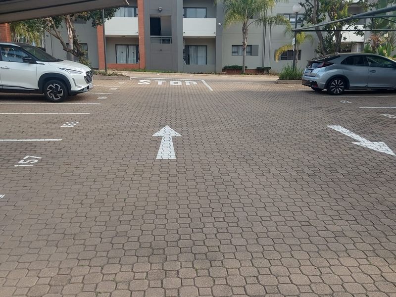 Exterior view of an apartment complex featuring a paved parking area with designated carports and building facade.