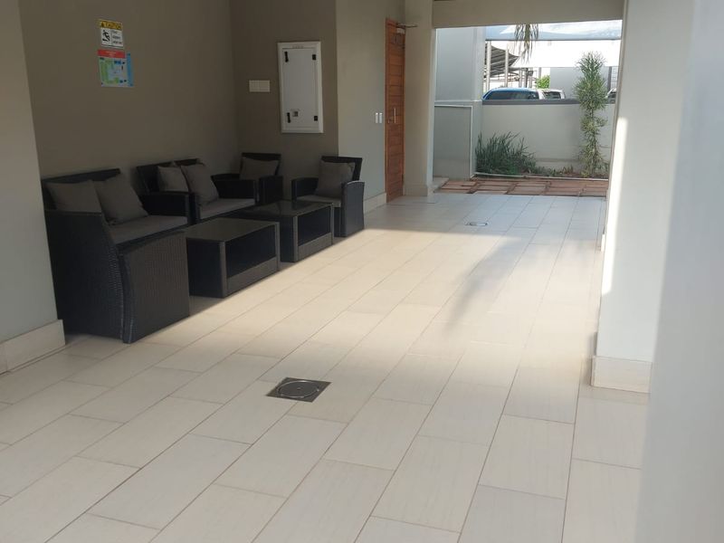 A covered outdoor patio area featuring modern tiled flooring, recessed ceiling lighting, and direct access to the exterior grounds.