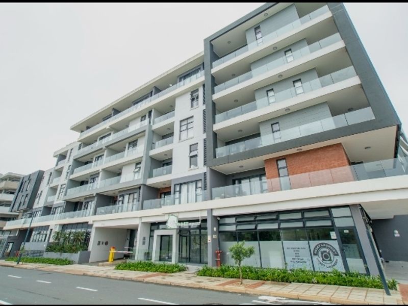 A modern multi-story apartment building featuring glass balconies, contemporary facade finishes, and ground-level commercial space with street-front access.