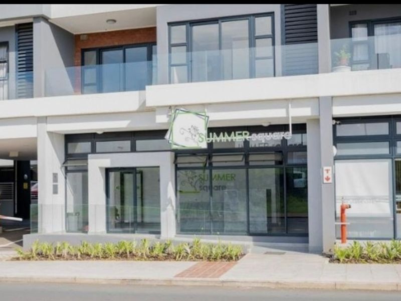 Modern apartment complex facade featuring glass balustrades, aluminium window frames, and a secure entrance with a boom gate and paved walkway.