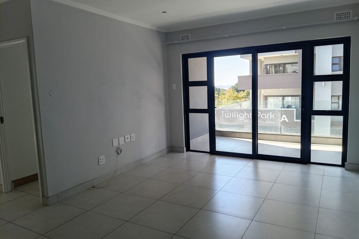 An empty, open-plan living area featuring neutral tiled flooring, recessed lighting, and large sliding glass doors leading to a private balcony.